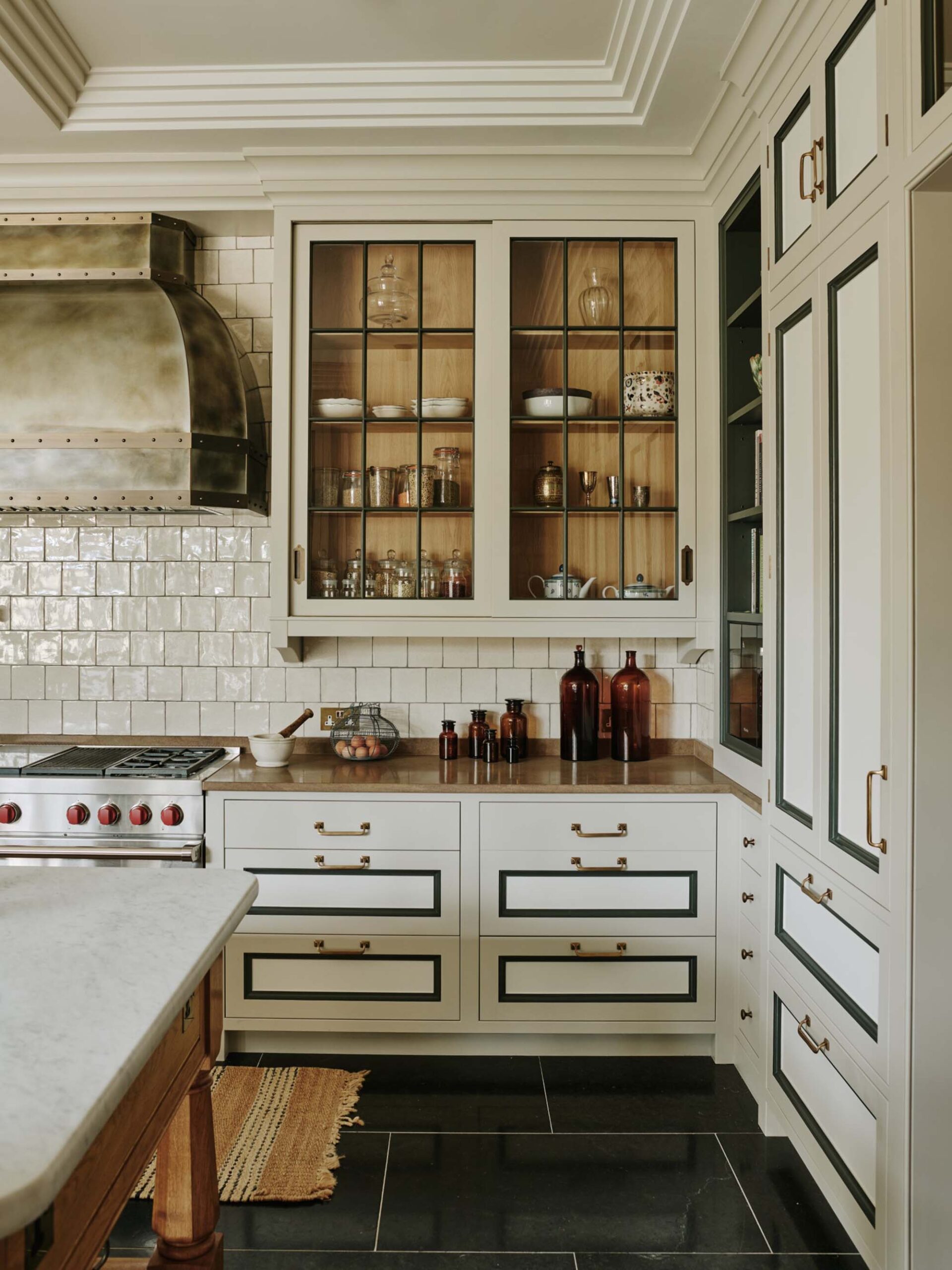 Art-deco-inspired-kitchen-cabinets-with-glass-doors-black-tile-floor-and-silver-range-hood