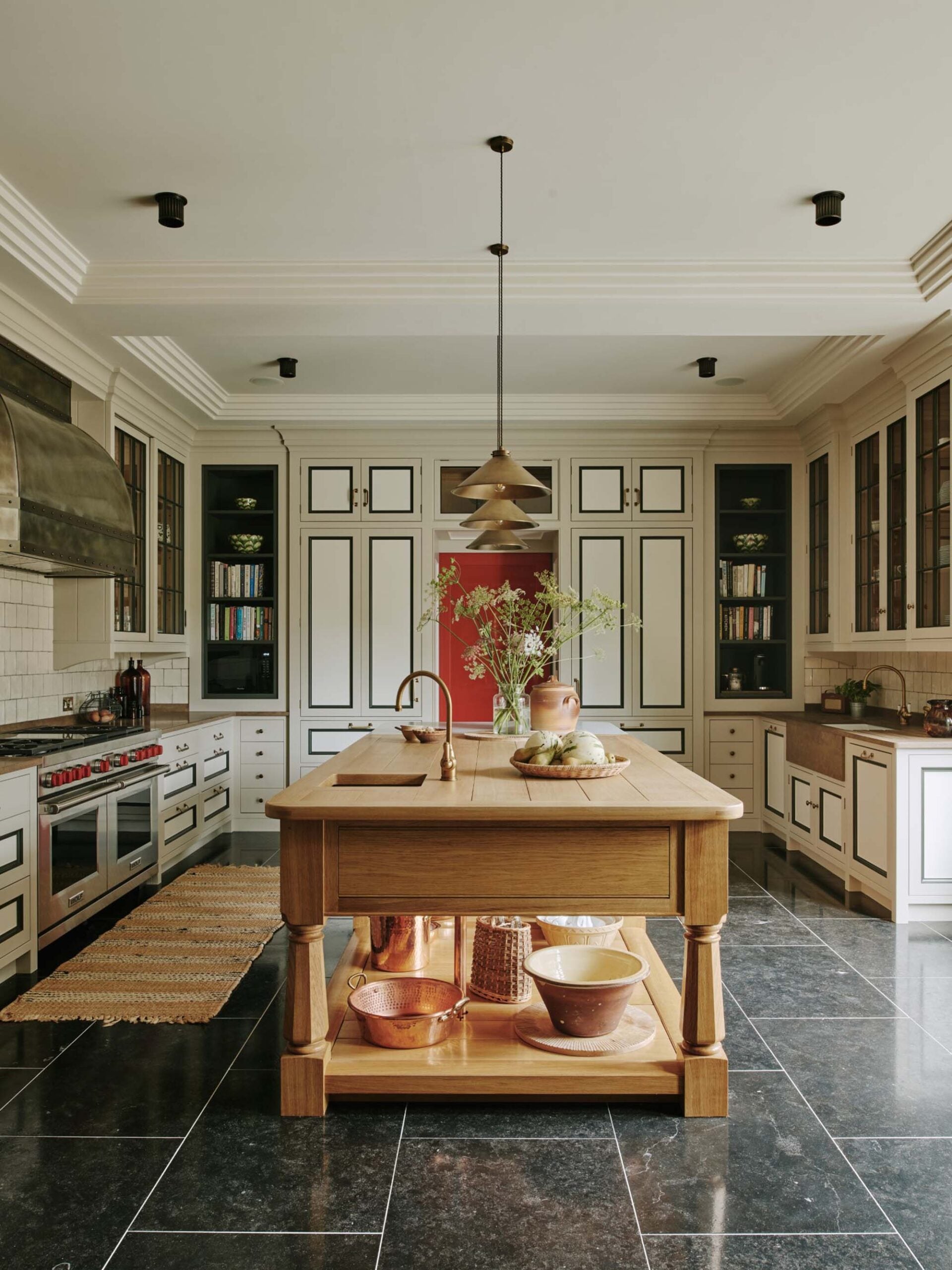 Art-deco-inspired-kitchen-with-wood-island-stainless-stell-range-and-hood-black-tile-floor-brass-hardware