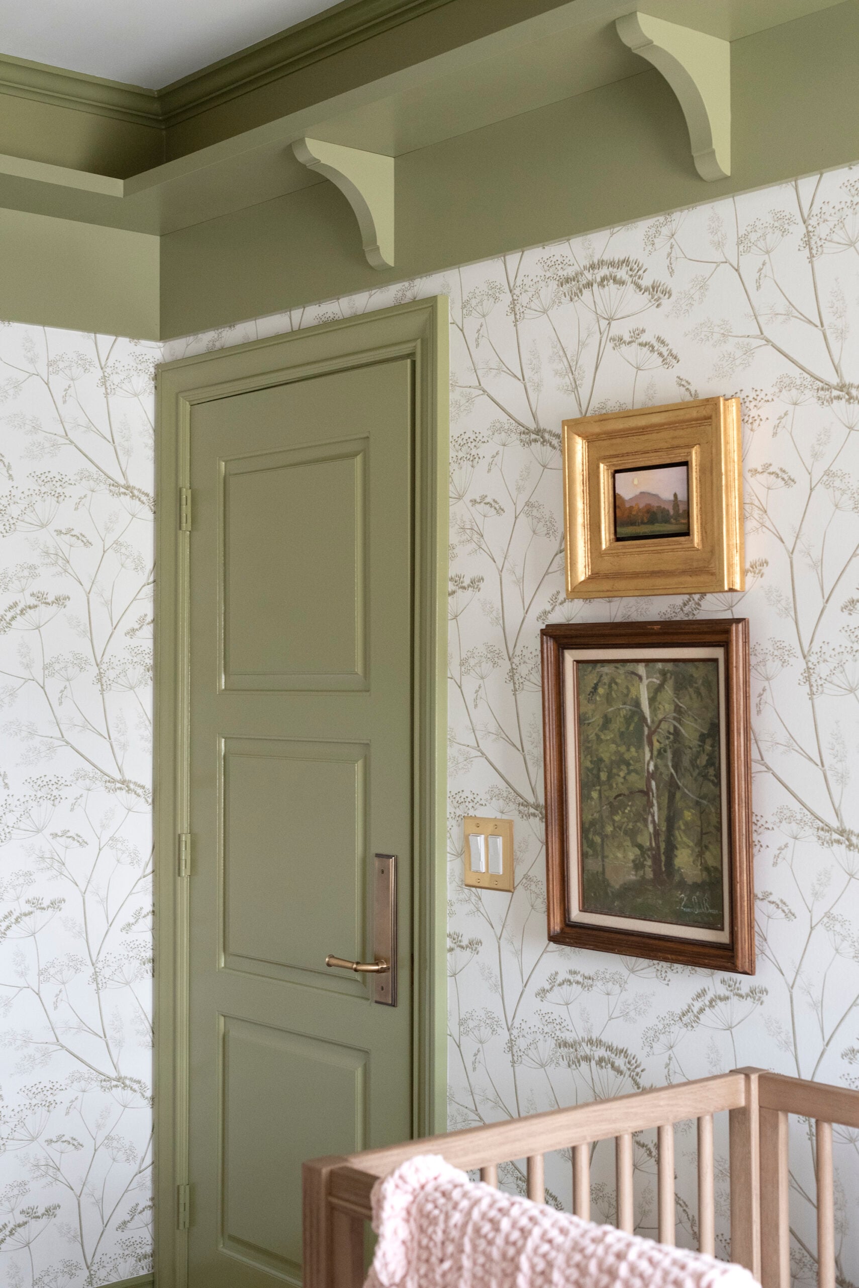 Stacked Oil Paintings in Nursery Next to Green Door Against Floral Wallpaper
