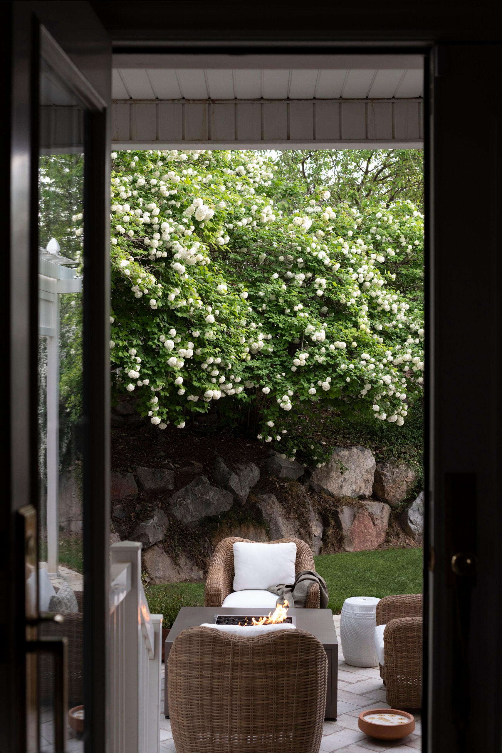 Woven Outdoor Chairs Around Fire Table on Patio With Viburnum in Background
