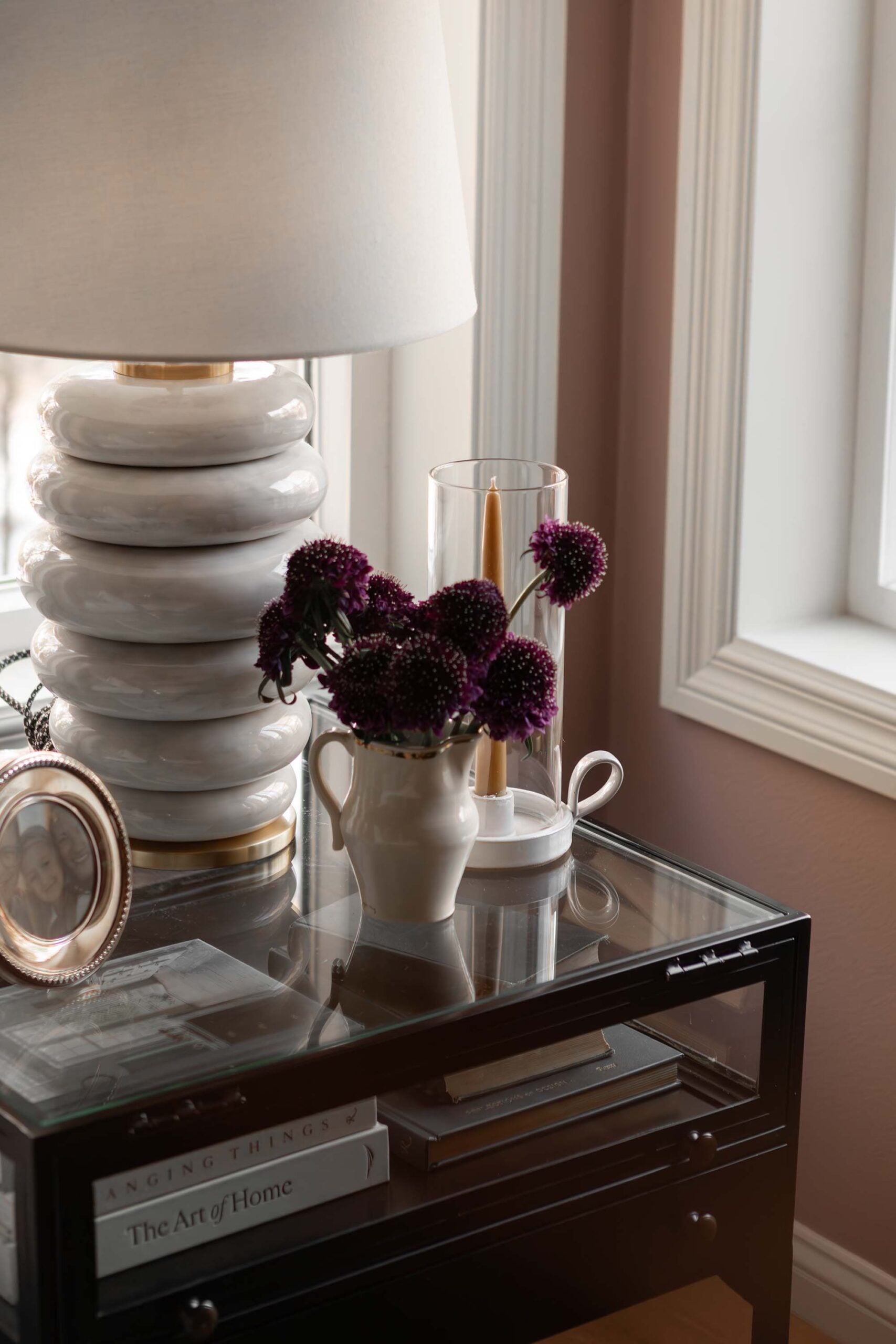 Oho Interiors-Carriage House-Bedside table in corner with windows styled with lamp photo and double handle vase of flowers