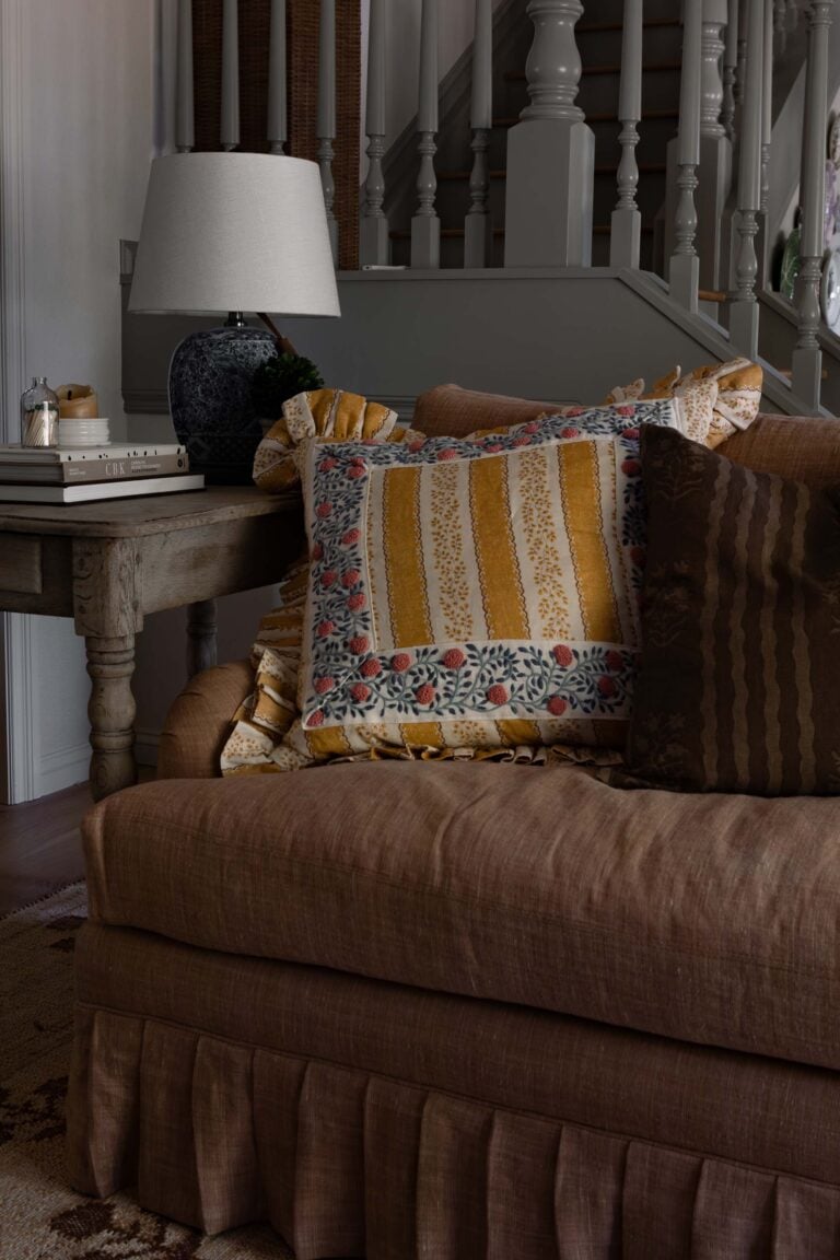 Oho Interiors-Carriage House-Skirted Sofa with Embellished pillows and wood side table by spindle staircase