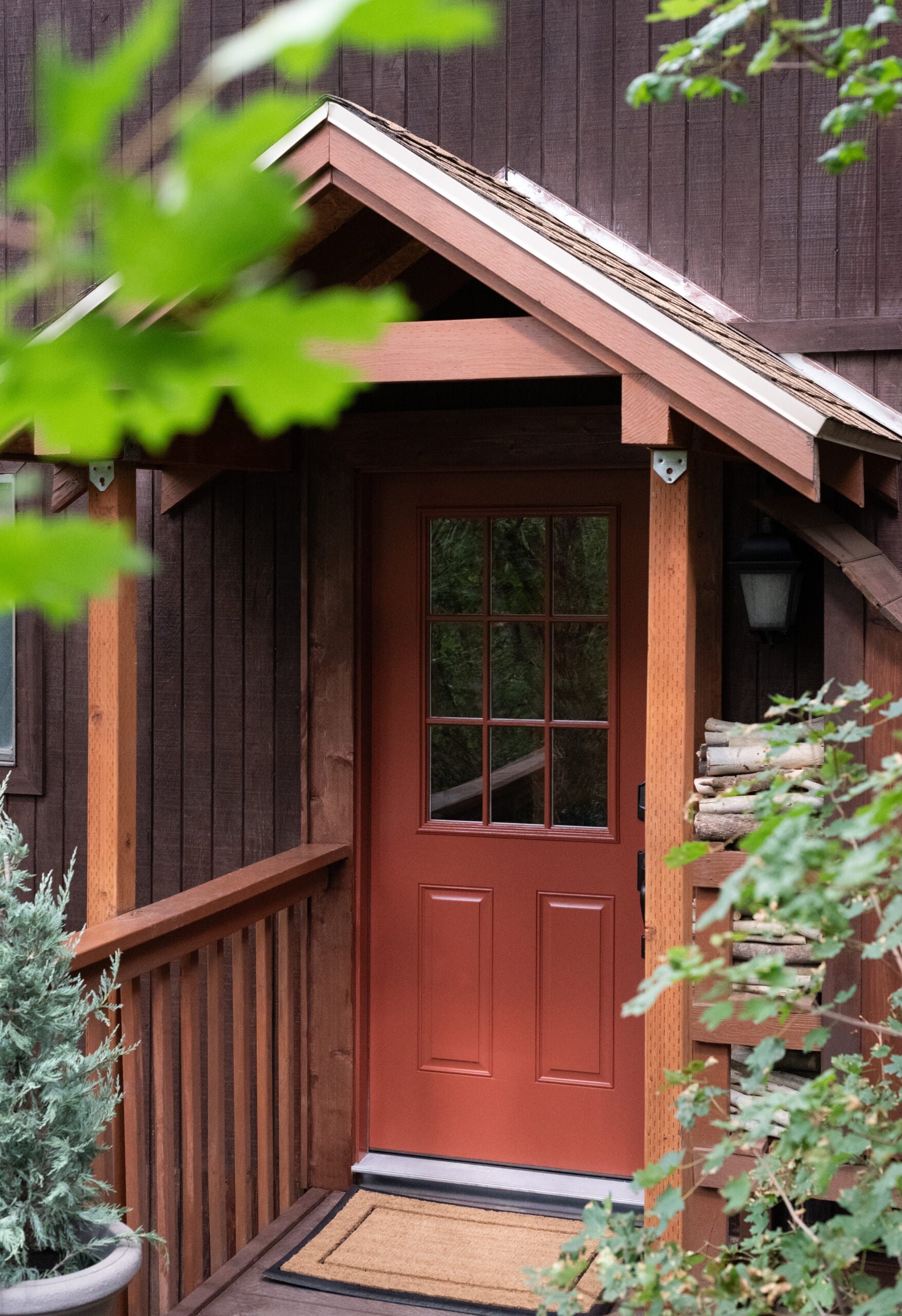 Red Cabin Front Door with Doormat, Planter, and Stacked Wood