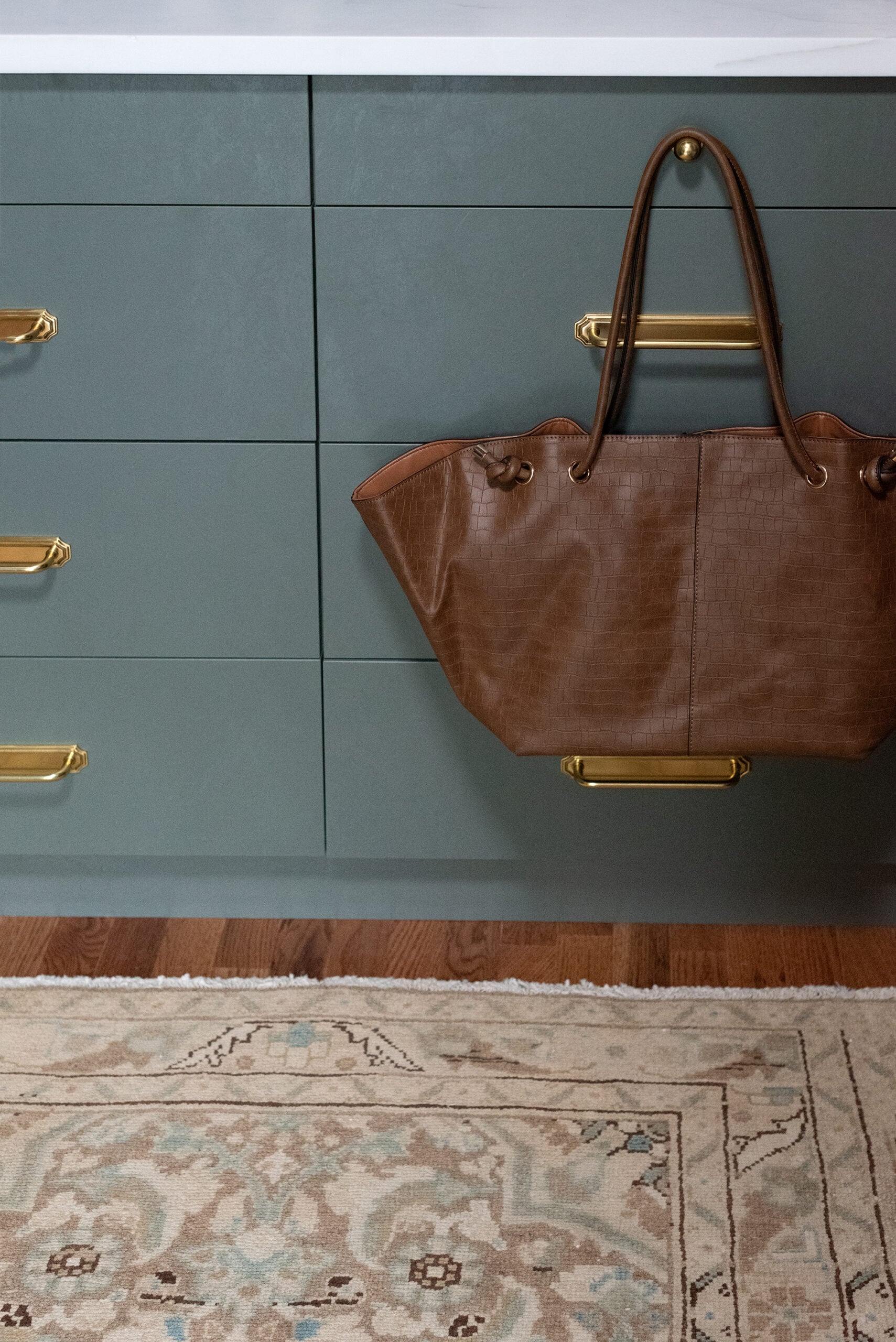 Leather Bag Hanging from Brass Knot in Walk-In Closet Against Teal Cabinets