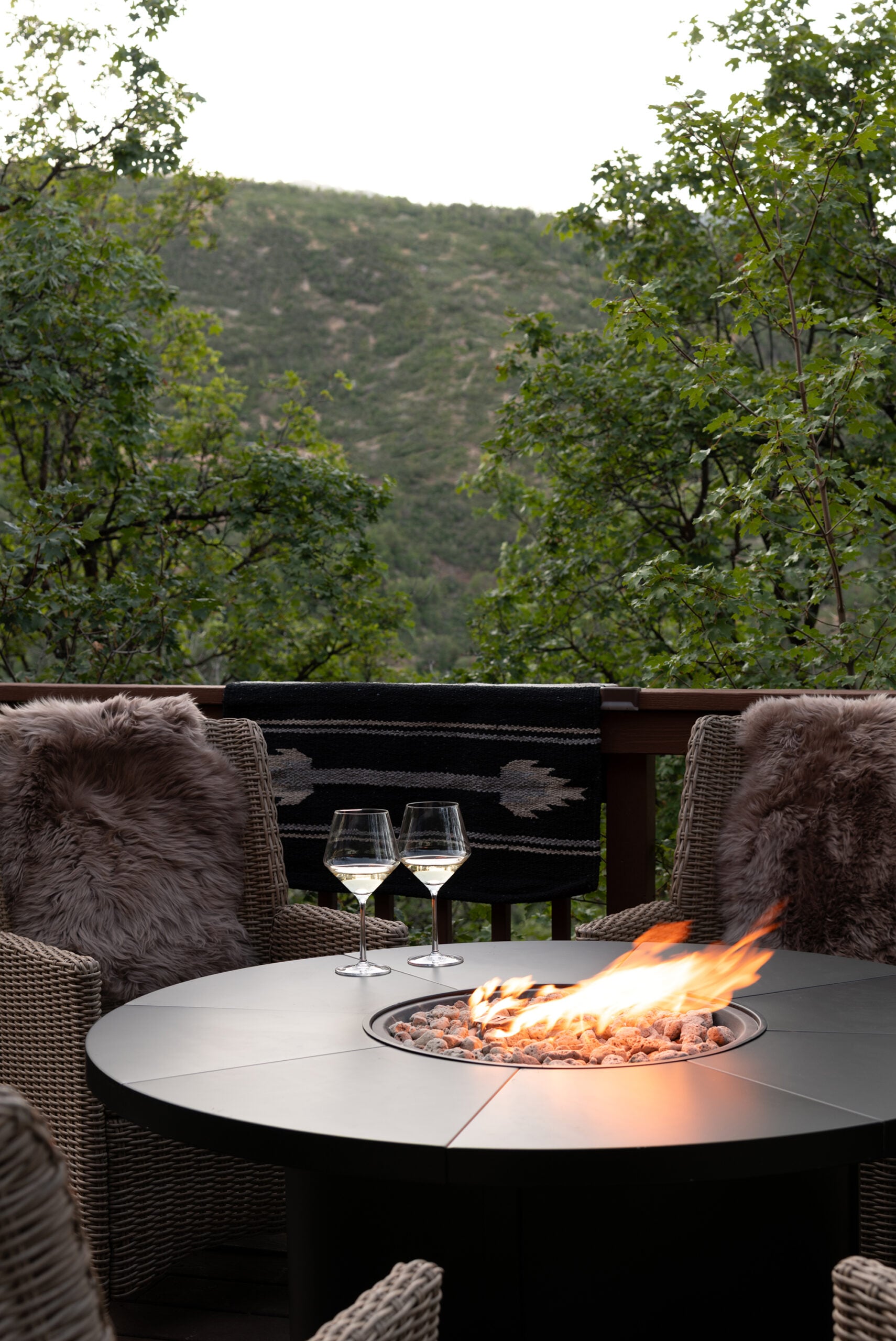 Two Wine Glasses on Fire Table with Woven Chairs at Mountain Cabin